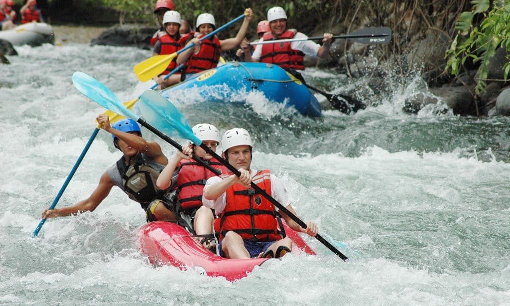 Costa Rica Rafting Image: Savegre River. Three rafts hold groups of people splashing, paddling, and smiling as they navigate the waters.