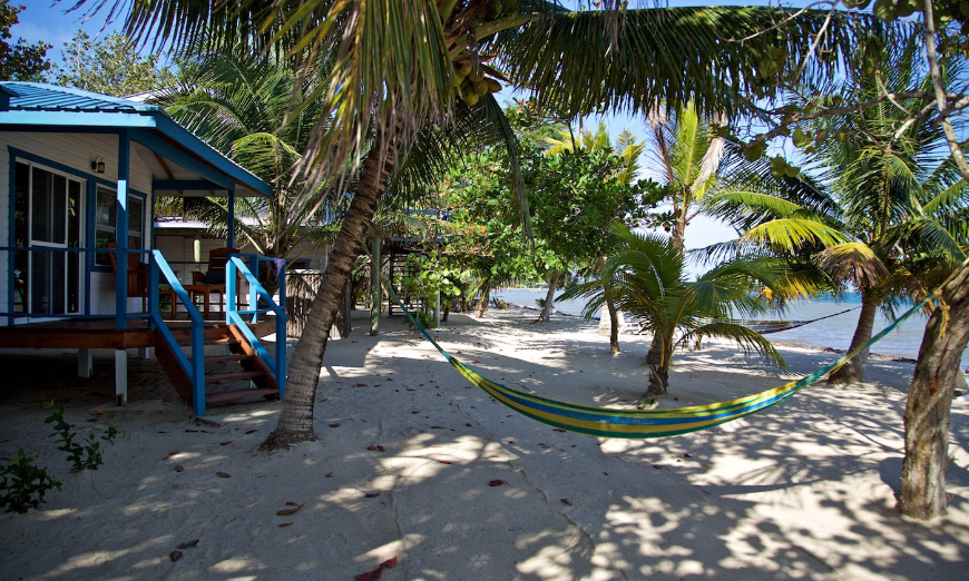 Best Beaches for Swimming in Belize Image: A colorful hammock hangs outside of a beach bungalow.