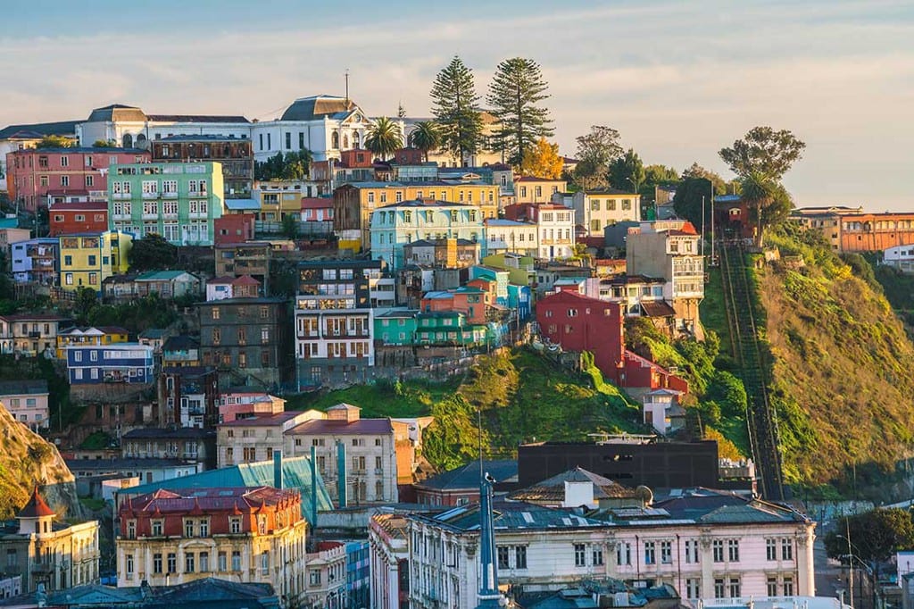 Destinations Worth Dreaming Image: Cubes of colourful buildings are present on a city hillside; the occasional green space or tree is present.