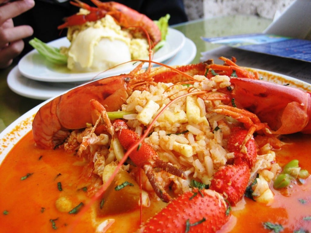 Visit Peru Image: The vibrant red seafood soup is piled onto a white dish; a generous scoop of rice has been placed in the middle of the dish.