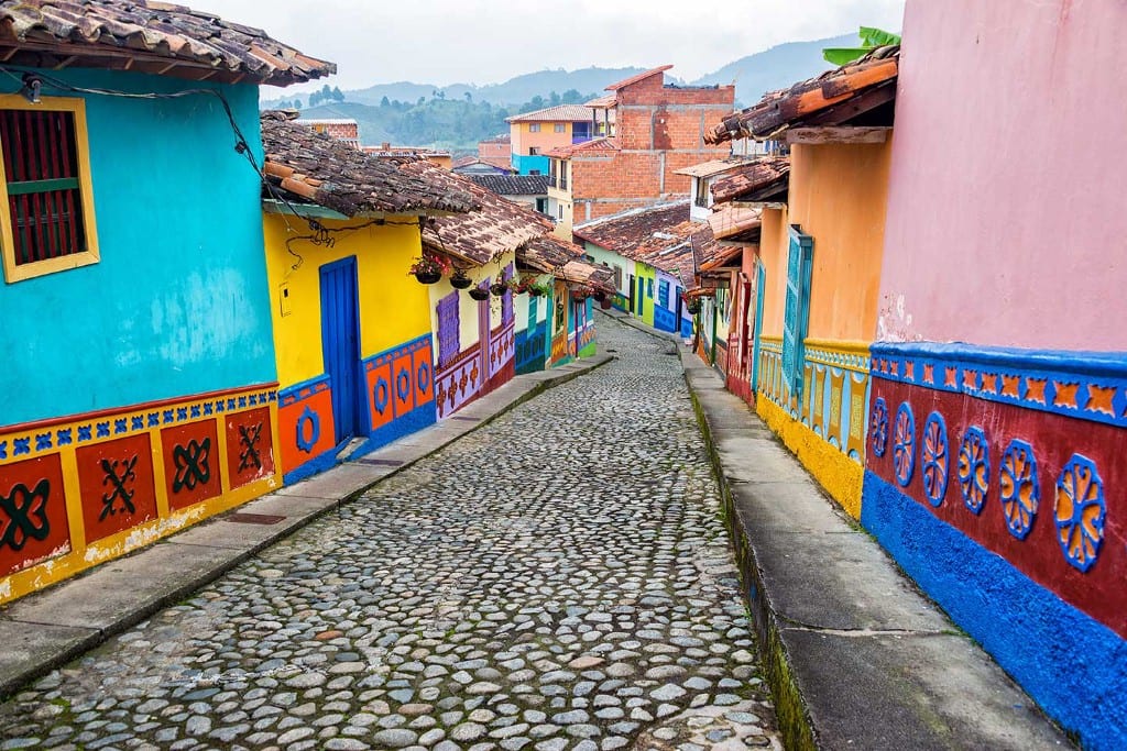 Destinations Worth Dreaming Image: Photograph of a camera looking down a cobblestone street; to the left and right are brightly coloured buildings with tiled roofs.