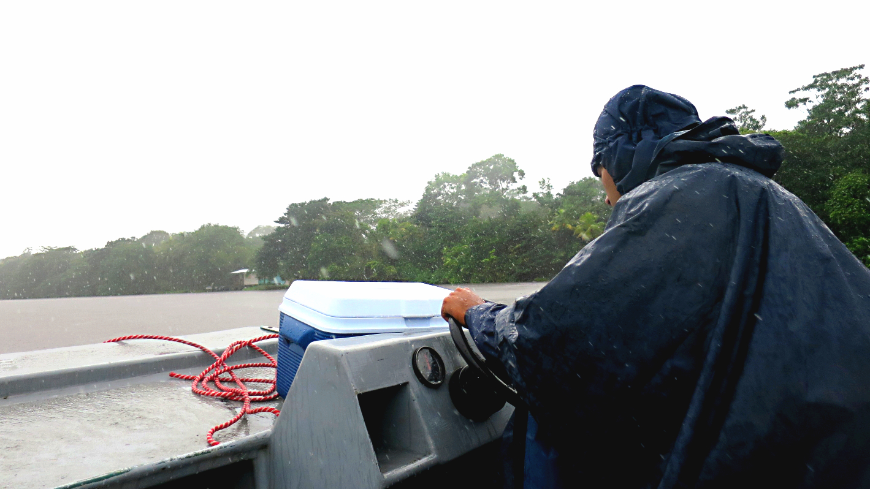 Costa Rica Tortuga Lodge Image: Tour guide Elvis has has back to the camera, and wears a black hooded poncho as he steers a boat in rain on a floating safari.