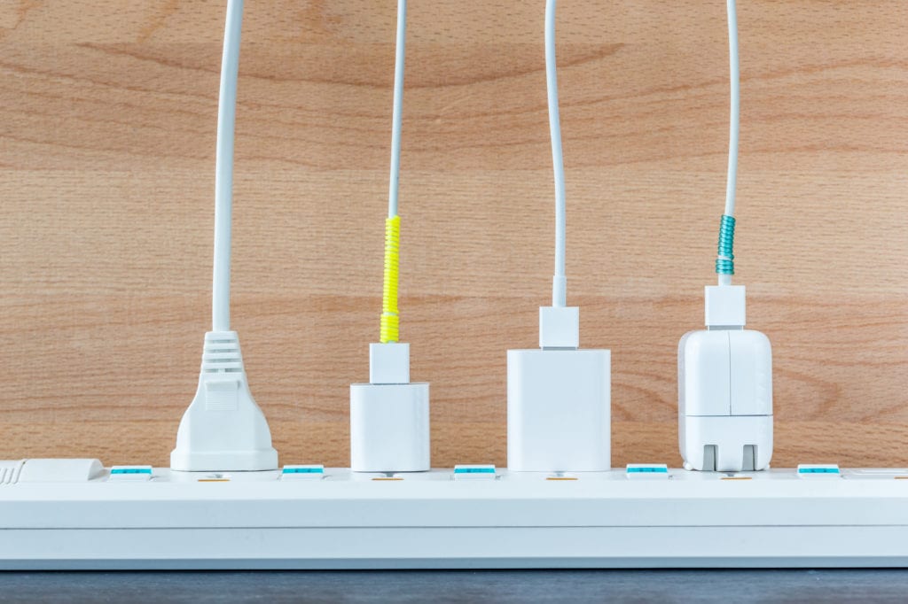 Family Adventure Image: Four different white chargers are plugged into a white power strip; two chargers have yellow and teal tape on them (respectively).