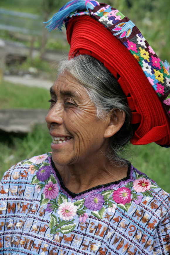 The Mayan civilization has taken on a new form... Mayans of Guatemala Image: An elder Guatemalan woman with silver hair smiles wearing an embroidered blouse and red hat.