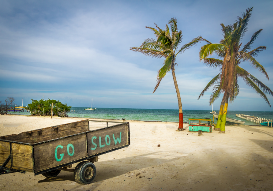 Moving to Belize Image: A wooden cart on a beach has "Go Slow" written on it.