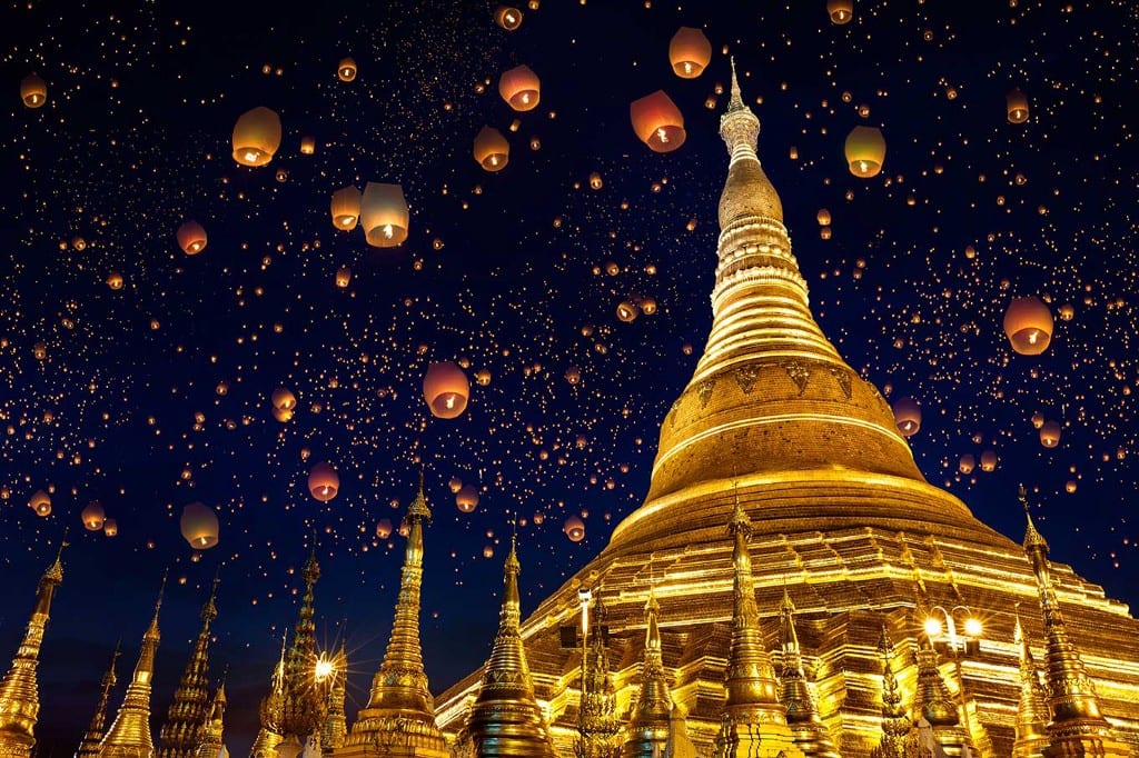 Destinations Worth Dreaming Image: Lanterns float up into the night sky past golden buildings.