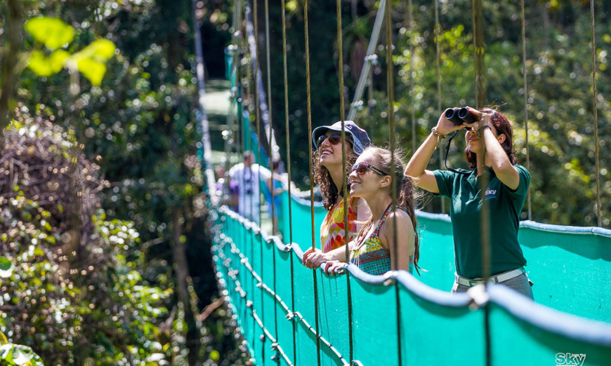 Is It Safe to Travel in Costa Rica Image: Three people stand on a turquoise suspension bridge.