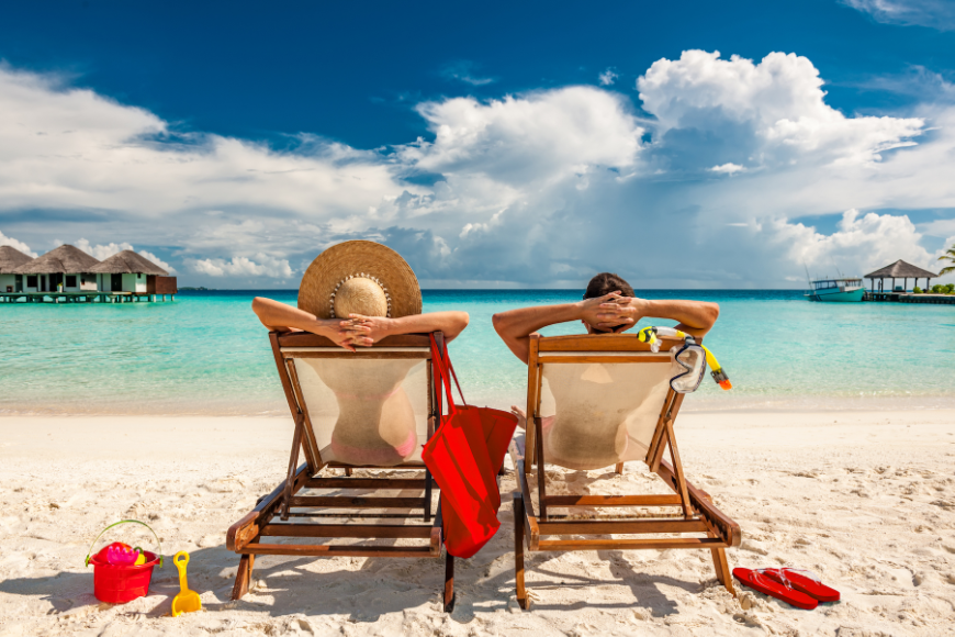 Is It Safe to Travel in Costa Rica Image: A male and female traveler sit in lounge chairs with their hands behind their heads on a beach.