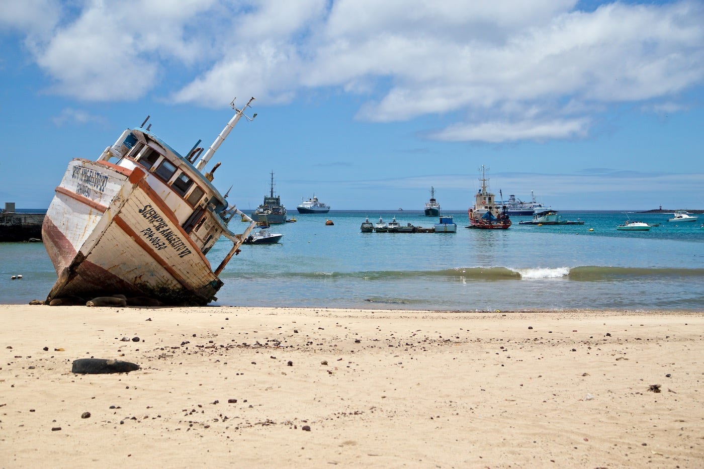 Photos Of The Galápagos Image: A ship run aground is tilted to one side on the shores of the Galápagos Islands; other ships are visible in the distance.