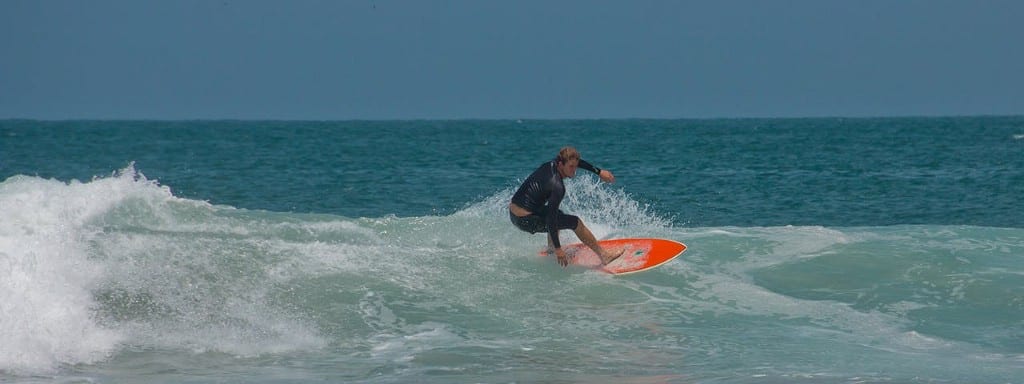 Best Surfing Beaches: A surfer in a black two piece wetsuit rides a red surf board in the water.
