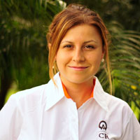 Tracy Rodriguez smiles whilst wearing a collard white shirt. Her chestnut and honey colored hair is pulled up.