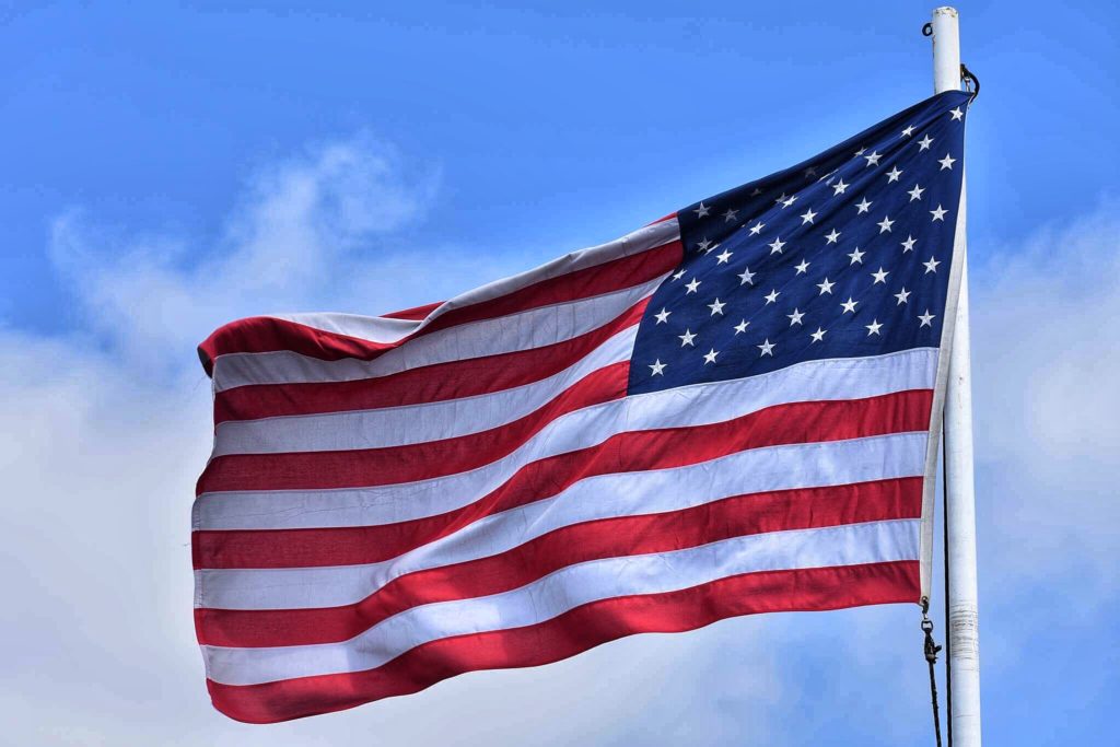 Legally Travel To Cuba Image: An American flag waves against the background of a cloud dappled blue sky.