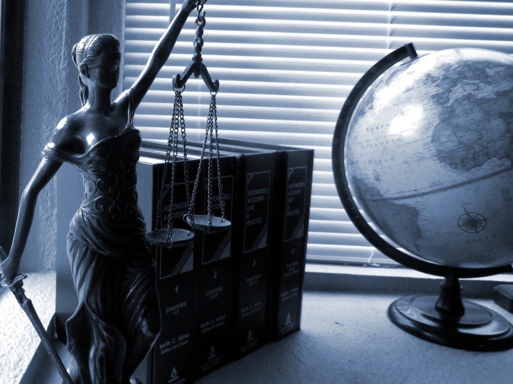 Legally Travel To Cuba Image: A black and white photo of the scales of justice, legal books, and a globe.