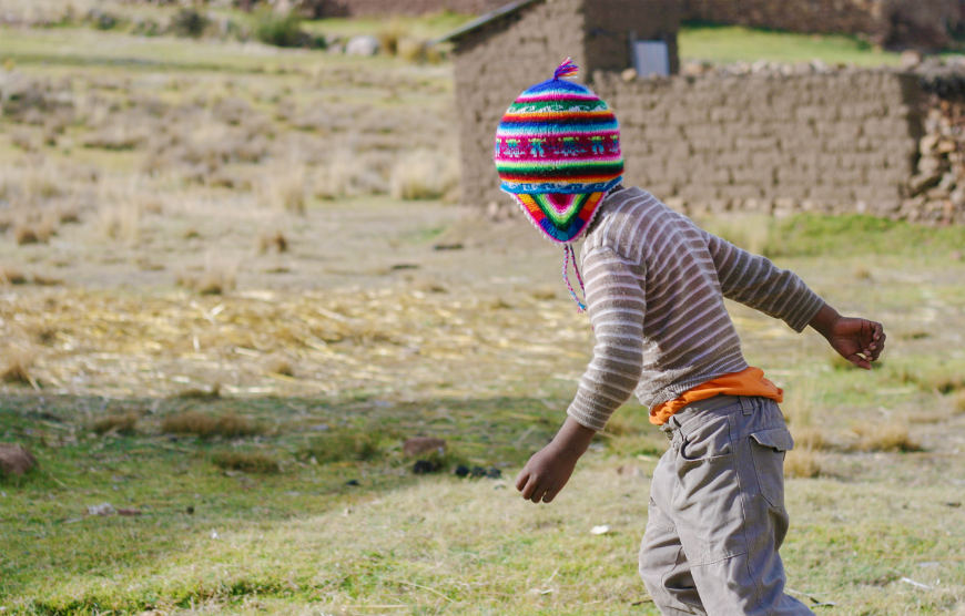 Bring home a chullo back to warm your head and your heart during colder months. Peru Souvenir Image: A little boy wearing cargo pants, and tan and white striped shirt is running through a field whilst wearing a rainbow coloured chullo hat.