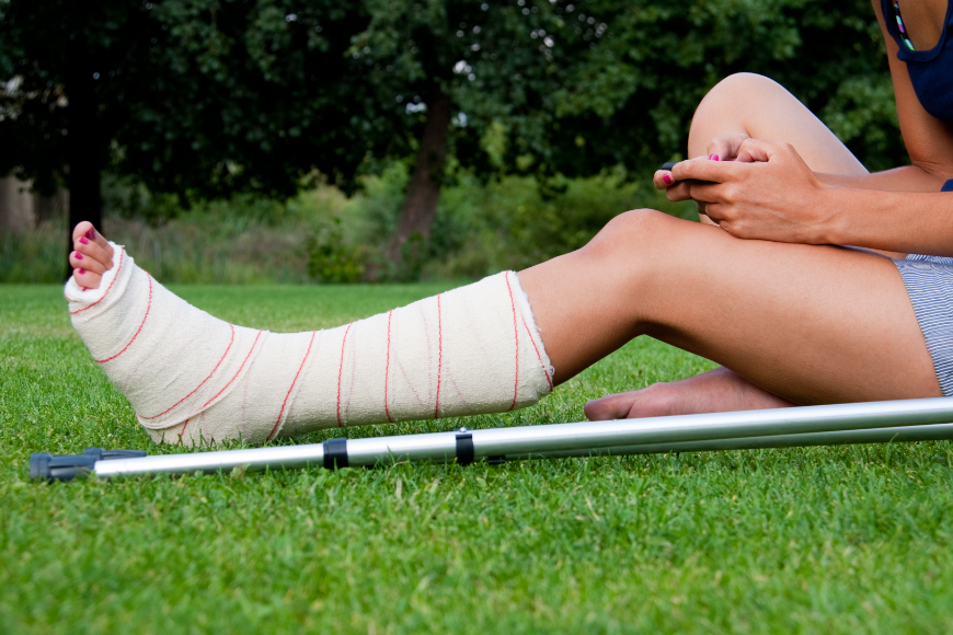 Travel insurance can help you rebook your vacation after you're done healing. Why Travel Insurance Is A Must Image: A woman sits in the grass using her phone. Her leg is broken and she has crutches.