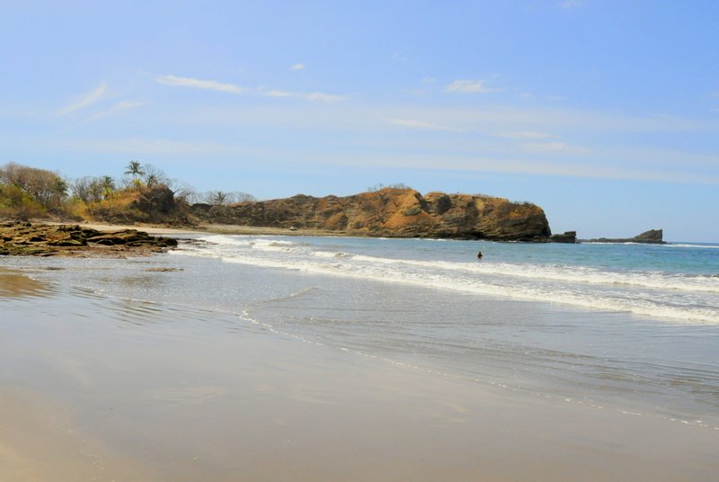 Shallow water and a rocky, forested headland at the end of a Nosara beach
