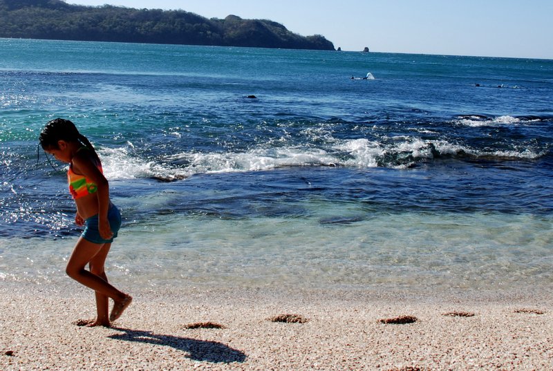 A girl walking on Playa Conchal's crushed-shell sand at the water's edge