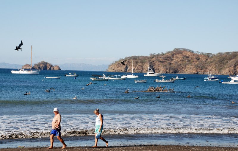 Two people walking the shoreline at Playas del Coco, with boats and islands behind
