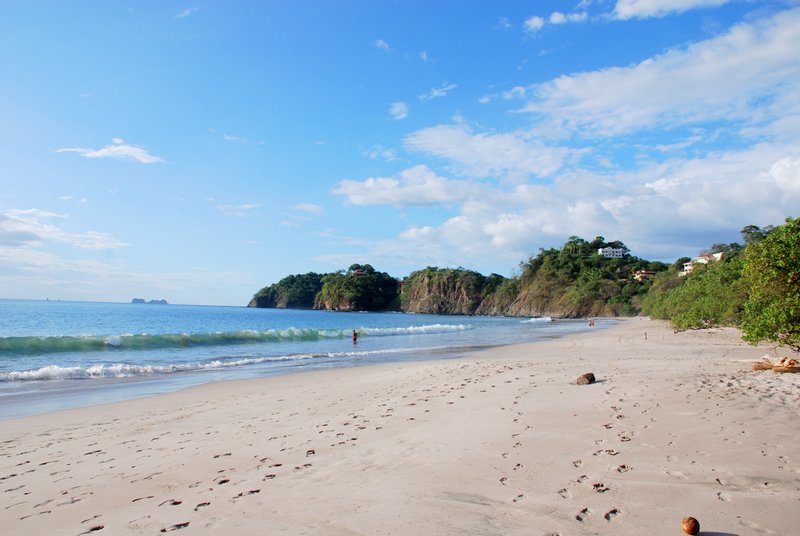 Footprints on the white sand of Playa Flamingo, with the headland behind